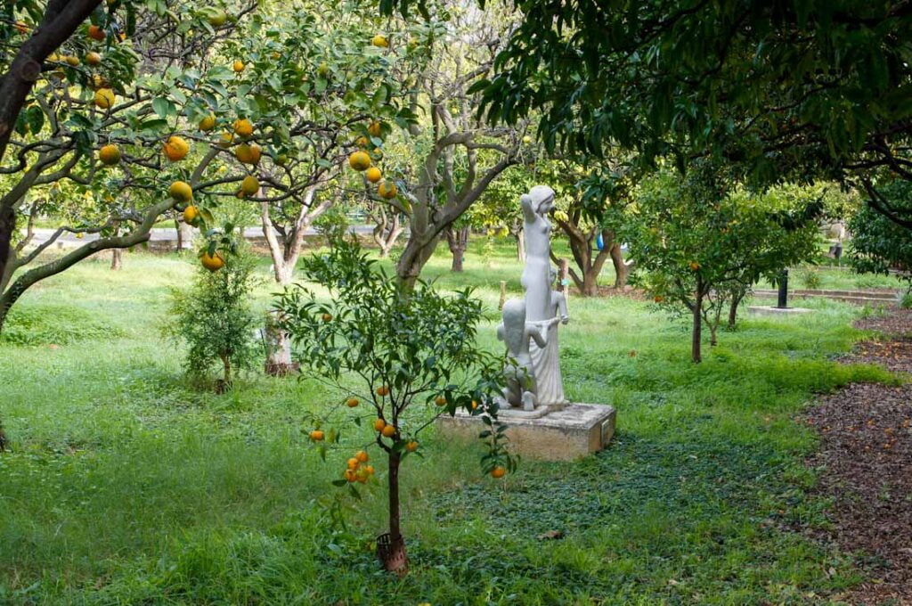 Weiße Statue einer Frau in wildem Garten mit Zitruspflanzen