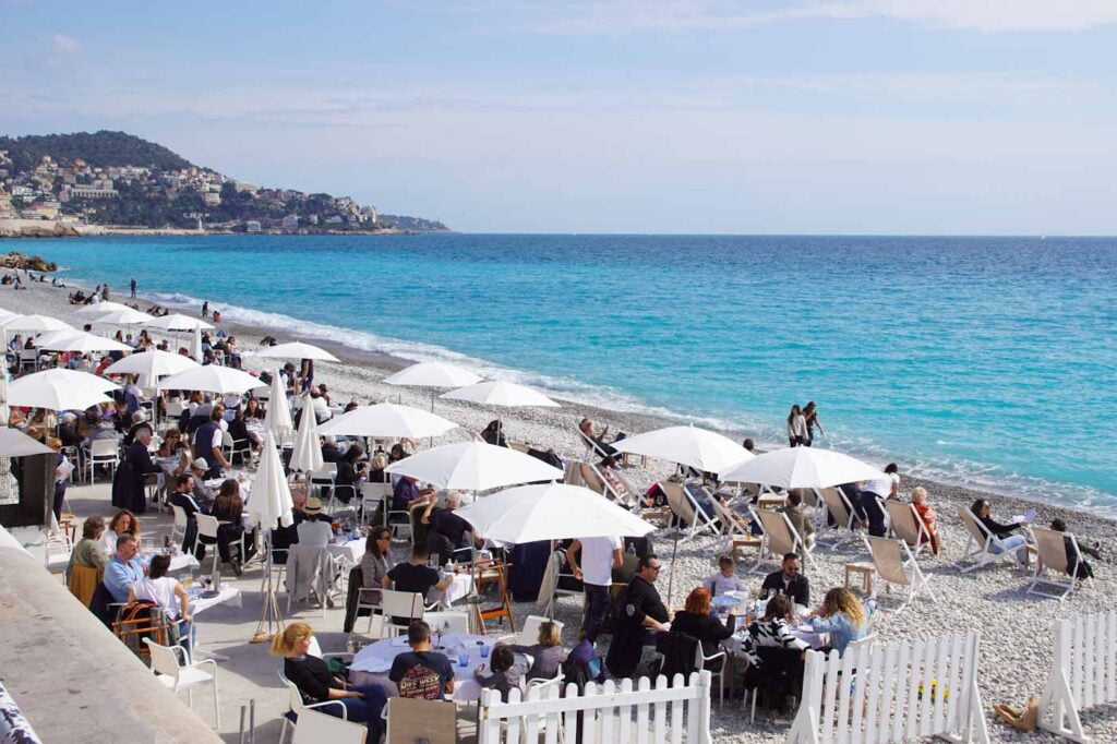 Beachclub Nizza mit weißen Sonnenschirmen vor türkisblauem Mittelmeer